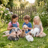 Three children sitting on grass holding and surrounded by fluffy rabbits in a garden